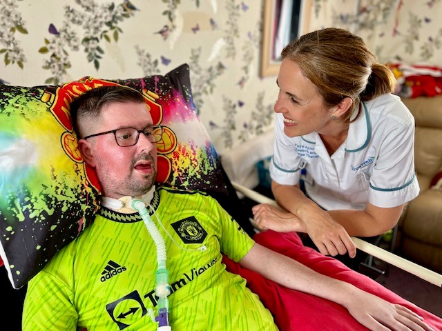 Steve wearing Manchester United kit with Faye Arnold at his bedside in white nurse uniform