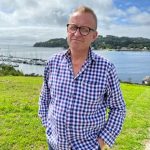 Andy in blue chequered shirt stood by River Tamar. Sunny day.