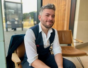 Man with beard and short hair sat in chair wearing 