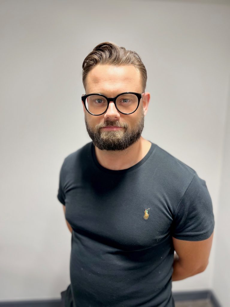 Man with short brown hair and glasses in black t-shirt