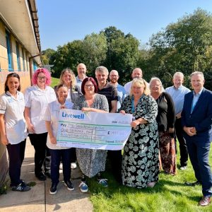 Group of people smiling at camera. Karen holding a giant cheque worth £1450.