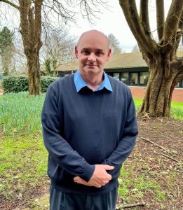 Mark stood outside Crownhill Court offices wearing a blue jumper and shirt