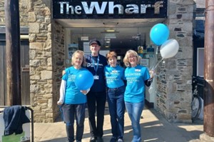 Four people stood outside The Wharf building. One is holding balloons.