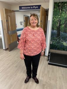 Woman in coral shirt and black trousers stood in ward corridor
