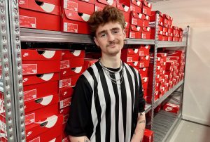 Young man with black and white sports top stood in stockroom full of shoe boxes