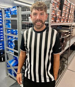 Man smiling in black and white striped sports top in storeroom full of shoe boxes