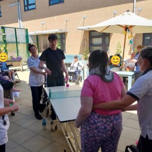 People playing table tennis in garden with people watching on