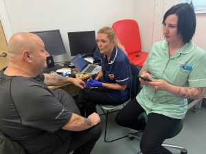 Two women in nursing uniform speaking with male patient in clinical setting