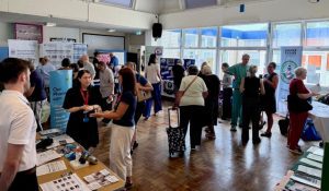 Groups of people talking to each other in large room, edged with information stands