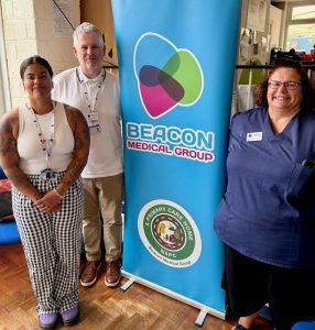 Two women and one man stood either side of an information banner saying Beacon Medical Group