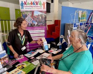 Woman stood behind an information desk talking to an older woman in a mobility scooter
