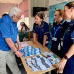Three women in blue nurses' uniform talking to an older man
