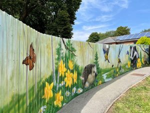 Nature artwork on fence featuring hedgehog, butterfly, badger and flowers.