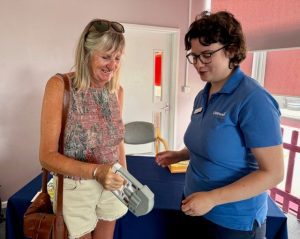 Woman holding grip machine, whilst woman in blue t-shirt watches