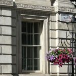 Downing Street sign on building with floral baskets hanging from a lamp post