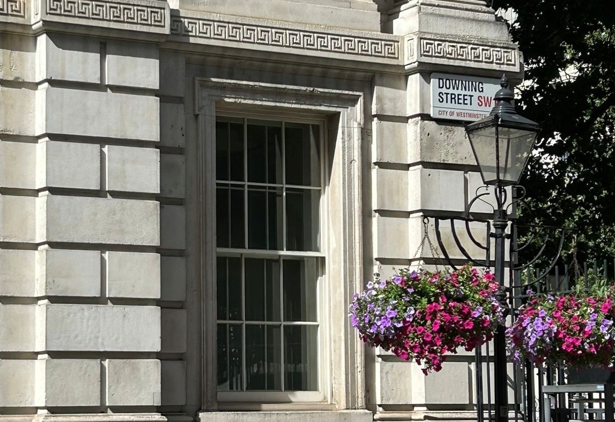 Sandra Pinch Downing Street July 2026 Downing Street sign on building with floral baskets hanging from a lamp post