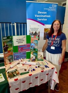 Woman stood by information desk wearing a t-shirt saying ask me about vaccines