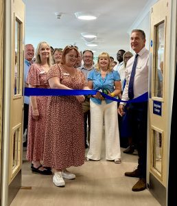 Woman in peach flowery dress cutting blue ribbon with people looking on